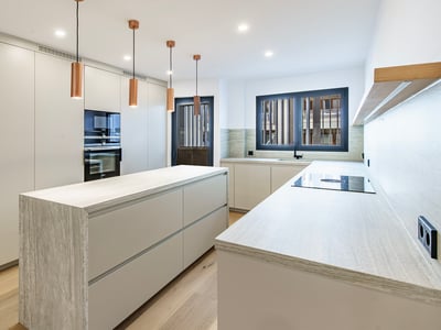 Modernt vitt kök med köksö i sten, pendellampor i koppar och trägolv.