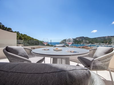 Mesa de terraza moderna con dos copas de vino frente a una vista espectacular del puerto y el mar bajo un cielo azul.