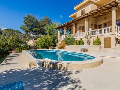 Großer privater Pool vor einer ockerfarbenen mediterranen Villa mit Terrasse und grünen Hügeln.