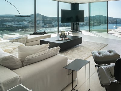 Modern living room with floor-to-ceiling windows, white sofas, a sleeping black cat, and a panoramic sea view.
