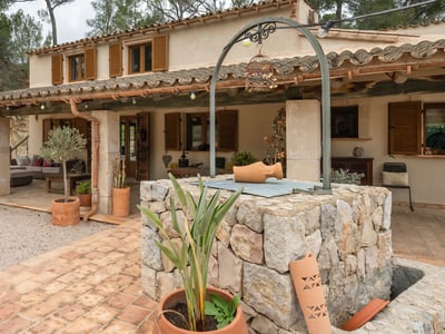 Facade of a rustic house with a covered porch, wooden shutters, and a stone well in the foreground.
