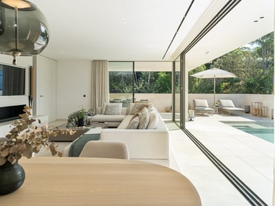 Salón moderno y luminoso con grandes puertas de cristal que dan a una terraza soleada y piscina privada.
