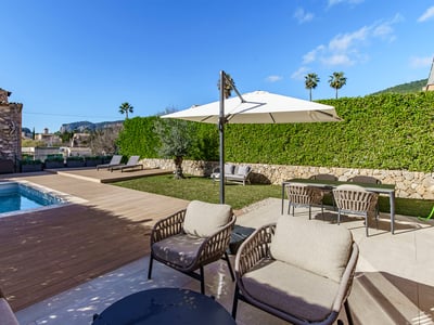Modern swimming pool with wooden deck, stylish outdoor furniture, and lush green hedges under a clear blue sky.
