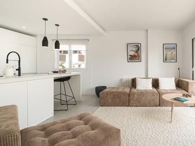 Bright living room with brown corduroy modular sofa, white textured rug, kitchen island, and large glass doors to a balcony.