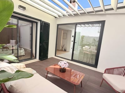 Outdoor patio with white pergola, wooden deck, terracotta-colored furniture, and tropical plants.