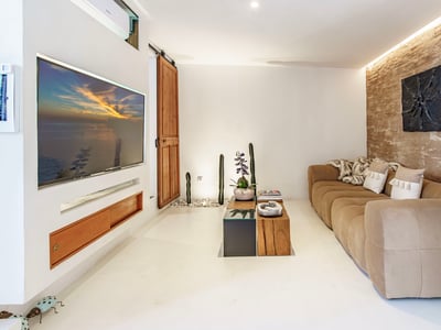 Living room featuring a beige sofa, rustic stone wall, built-in television, and Mediterranean decor elements.