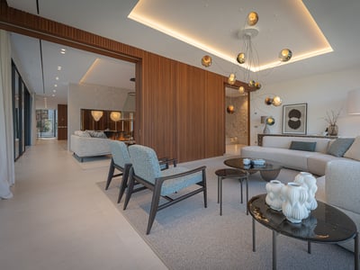 Modern living room with a large gray sofa, blue armchairs, wood slatted wall, and a unique glass orb chandelier.