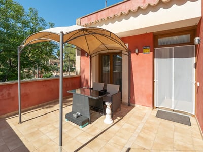 Terraza soleada con paredes de color terracota, suelo de baldosas y un cenador con mesa y sillas.