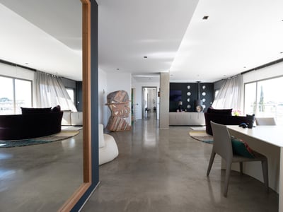 Bright interior with polished concrete floors, a large mirror reflecting a sofa, and contemporary art sculptures.