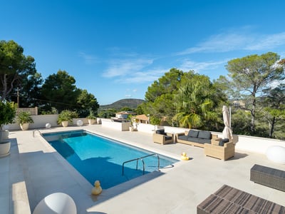 Rektangulär blå pool på vit stenterrass med utemöbler och utsikt över medelhavsgrönska.