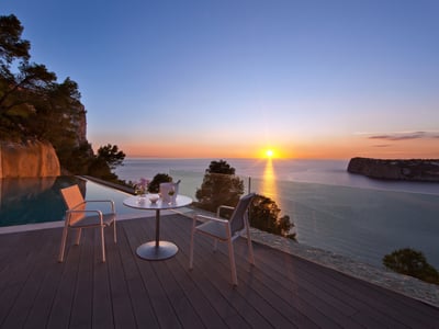 Solnedgång från en lyxig terrass med infinity-pool, trädäck och vita moderna utemöbler.