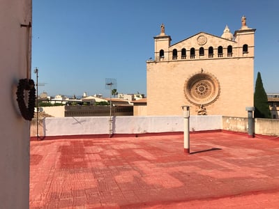 Rote Dachterrasse mit Blick auf eine steinerne Kirchenfassade mit Rosettenfenster unter blauem Himmel.