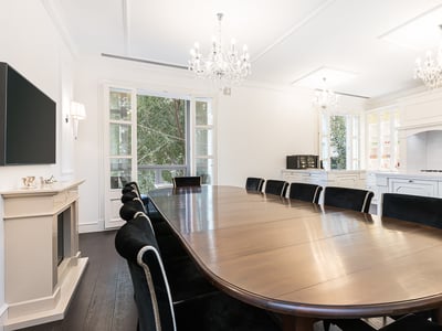 Großer Esstisch aus Holz mit schwarzen Samtstühlen unter Kristalllüstern in einem hellen, weißen Raum mit Kamin.