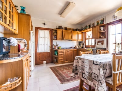 Helle rustikale Küche mit Holzschränken, einem Esstisch mit gemusterter Tischdecke und natürlichem Licht.