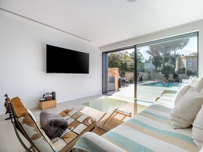 Salón luminoso con sofá a rayas, televisor grande y puertas de cristal que dan a una terraza con piscina.