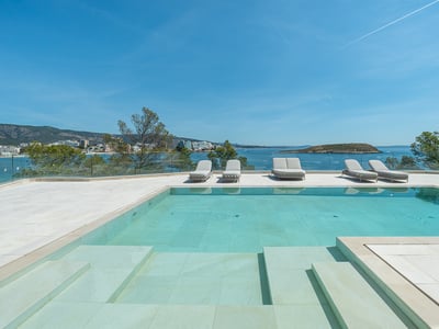 A turquoise swimming pool on a stone terrace with sun loungers overlooking the Mediterranean sea and a distant island.