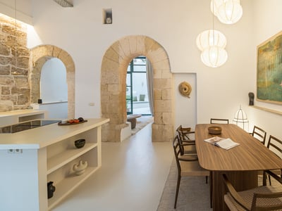 Salle à manger contemporaine avec table en bois sous des suspensions globes, encadrée par des arches en pierre.