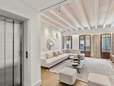 Amplio salón moderno con un sofá rinconera blanco, vigas de madera en el techo y acceso por ascensor privado.