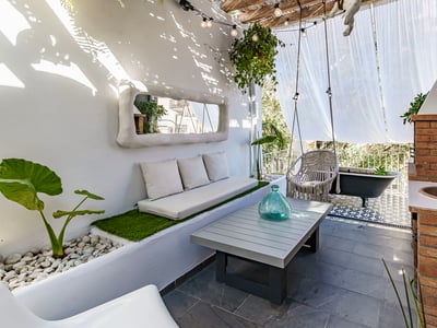 Sun-drenched white terrace with built-in sofa, macrame swing, brick outdoor sink, and a black clawfoot bathtub.