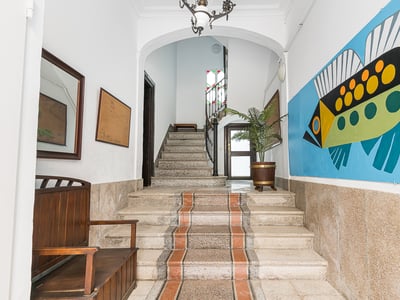 Eingangsbereich mit Steintreppe, Holzbank und einem großen farbenfrohen Fisch-Wandbild an der Wand.