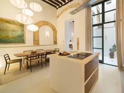 Cuisine moderne avec îlot, table à manger, suspensions boules en papier et arches en pierre apparente.