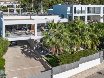 Vista arquitectónica de una villa moderna blanca con terrazas, palmeras y muros de piedra bajo luz solar intensa.