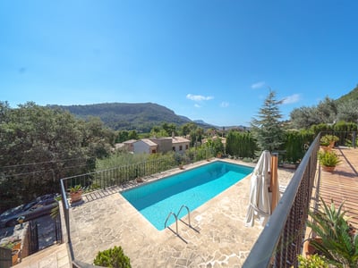 Piscina rectangular rodeada de terraza de piedra con vistas panorámicas a las montañas bajo un cielo azul despejado.