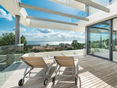 Chaises longues sur une terrasse en bois avec garde-corps en verre surplombant la mer, à côté d'une salle à manger ouverte.