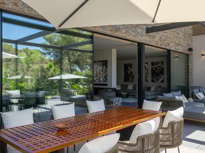 Modern terrass med ett stort träbord, grå soffor och skjutdörrar i glas som leder till vardagsrummet.