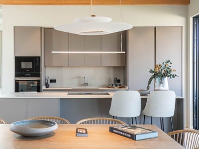 Cocina contemporánea con armarios color topo sin tiradores, isla central con taburetes y elegantes lámparas colgantes.