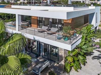 Vista aérea de una villa moderna blanca de dos plantas con balcones de cristal y palmeras tropicales exuberantes.