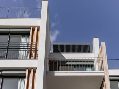 Froschperspektive eines modernen weißen Gebäudes mit Metallgeländern und Holzlamellen unter blauem Himmel.