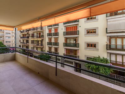 Bred stenterrass med metallräcke och orangea markiser med utsikt över bostadshus.