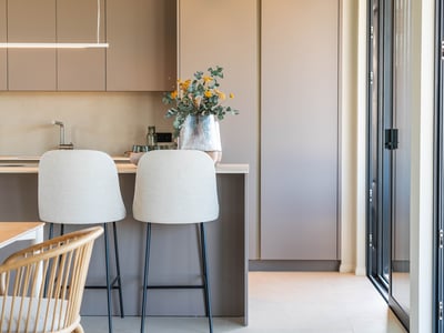 Una cocina moderna con armarios topo mate, una isla con dos taburetes claros y una viga de madera en el techo.