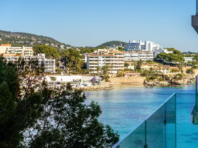Vista elevada de una bahía turquesa con edificios blancos y puerto deportivo desde un balcón de cristal.
