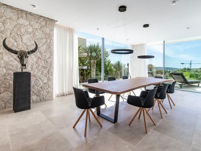 Comedor moderno con mesa de madera, sillas negras, pared de piedra con escultura y grandes ventanales.