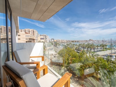 Modern balcony with wooden armchairs and glass railing overlooking a panoramic marina with yachts and city buildings.