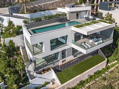 Vue aérienne d'une villa blanche à trois niveaux avec piscine à débordement sur le toit et balcons en verre.