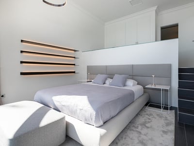 Modern bedroom featuring a gray bed, integrated LED wall shelving, and minimalist white interior.