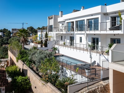 Modern white multi-level villa with a rectangular swimming pool, wooden decking, and lush Mediterranean landscaping.