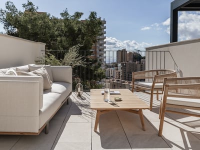 Luxuriöse Dachterrasse mit cremefarbenem Sofa, Holzsitzbänken und Blick auf die Stadt und das Meer unter blauem Himmel.