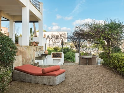 Terraza con tumbona naranja, barbacoa de obra y comedor bajo pérgola con vistas al campo.