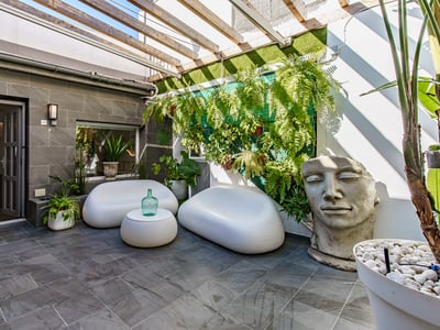 Contemporary patio with white curved sofas, stone tiles, wooden pergola, and a large stone face sculpture.