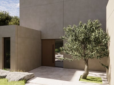 Modern villarentré med beige betongväggar, trädörr och ett olivträd på en stenlagd innergård.
