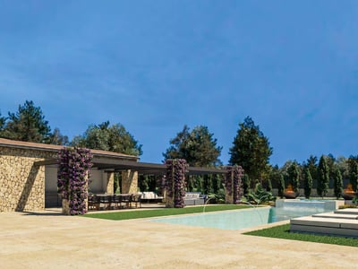Piscina moderna con arquitectura de piedra, flores púrpuras, braseros y tumbonas bajo un cielo azul despejado.