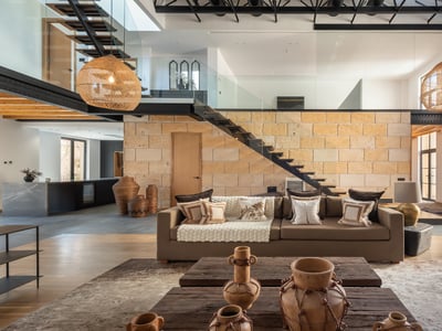 Modernes Wohnzimmer mit Steinwand, schwebender Treppe, großen Weidenlampen und einem bequemen braunen Sofa.