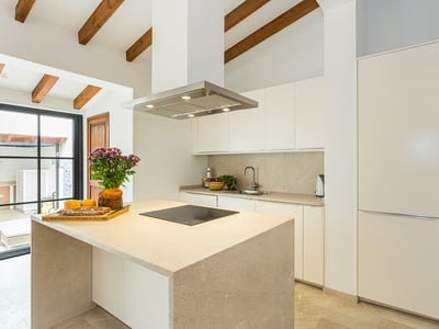 Bright kitchen featuring a stone island, exposed wooden ceiling beams, and minimalist white cabinetry.