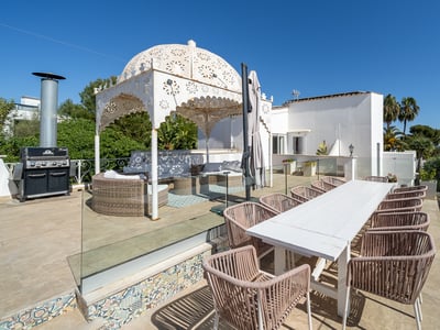 Spacious terrace with a white dining table, wicker chairs, BBQ station, and an ornate white gazebo under a clear blue sky.