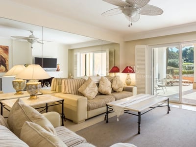 Ein helles Wohnzimmer mit cremefarbenen Sofas, einem großen Wandspiegel und Glasschiebetüren zu einer sonnigen Terrasse.