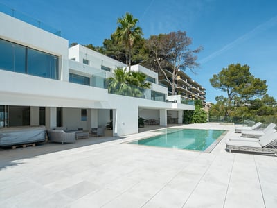 Modern white villa with a rectangular swimming pool, grey sun loungers, and glass railings under a clear blue sky.